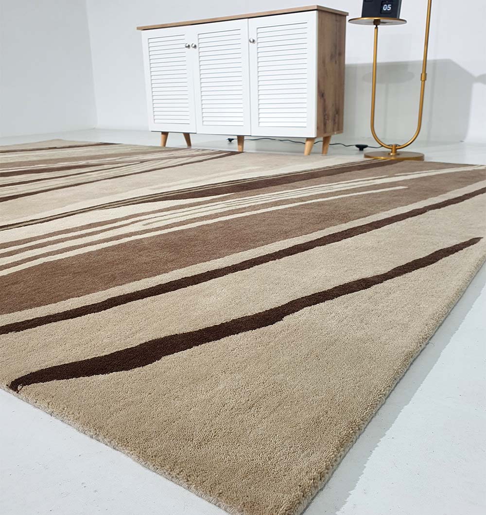 The RAMSHA HOME Striking Pattern Home Decor Handmade Carpet – HTW-61, featuring beige and brown abstract stripes, is displayed on a white floor in front of a white cabinet with wooden legs near a floor lamp.