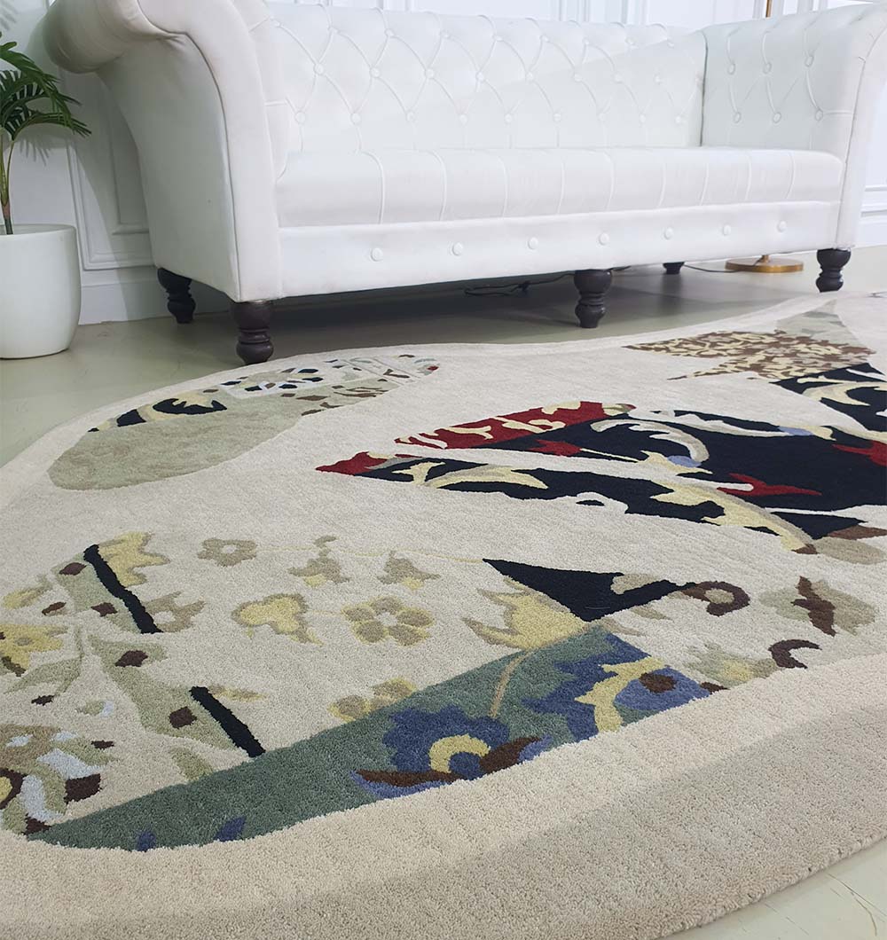 The Unique Unshaped Handmade Carpet For Home Decor HTW-70 by RAMSHA HOME, featuring abstract beige, black, red, and blue designs, is placed on a light floor in front of a white tufted sofa in a modern room with a potted plant.
