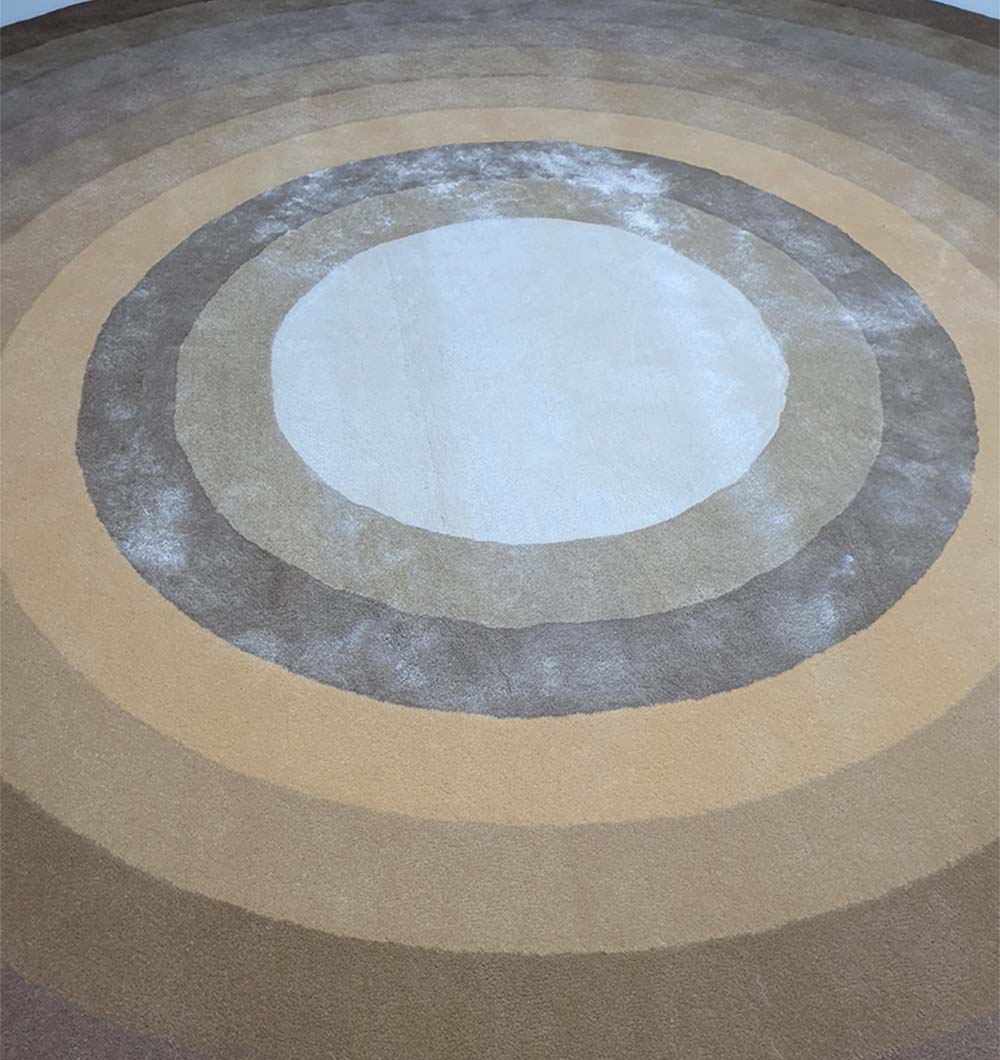 The RAMSHA HOME Multi Color Handmade Hand Tufted Carpet HTWV-49 is a round wool rug with concentric circles in beige, tan, brown, and cream for a gradient look, adding warmth and texture to any room.