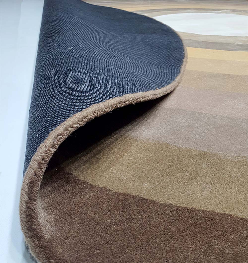 A close-up of the RAMSHA HOME Multi Color Handmade Hand Tufted Carpet HTWV-49 shows one corner lifted to reveal its black non-slip backing, highlighting its brown and beige tones.