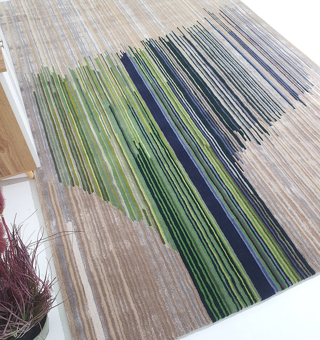 The RAMSHA HOME Striped, Beige & Grey Rug with Navy & Green Accent Bands – HTWV-52 features a modern abstract design. Part of a wooden table and a vase with reddish plants can be seen at the edges.