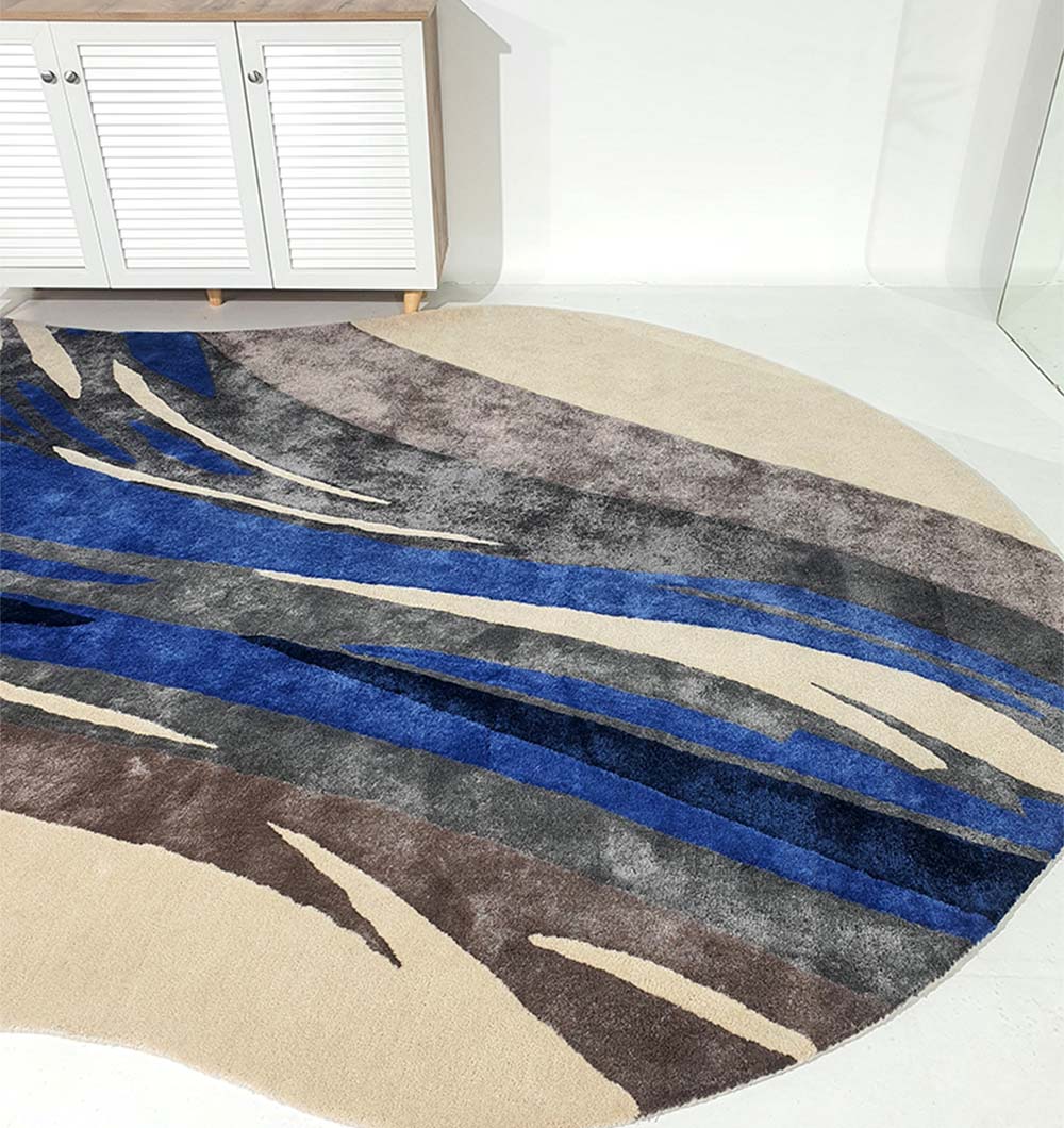The RAMSHA HOME Irregular Shape Hand-Tufted Carpet HTWV-69, featuring abstract waves in blue, gray, beige, and brown wool-viscose, is placed on a light floor before a white shutter-door cabinet in a minimal modern setting.