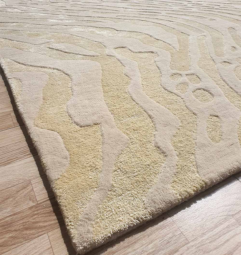 Close-up of the RAMSHA HOME Handmade Multi Color Carpet For Home Decor HTWV-75, showcasing its beige and cream hand-tufted, wavy abstract pattern and textured raised design on a light wood floor for added depth and style.