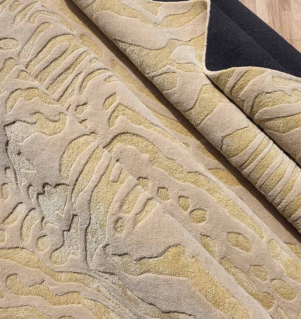 A close-up of the RAMSHA HOME Handmade Multi Color Carpet For Home Decor HTWV-75 shows its abstract wavy beige and light brown wool patterns, hand-tufted texture, partially folded to reveal a black backing and wooden floor.