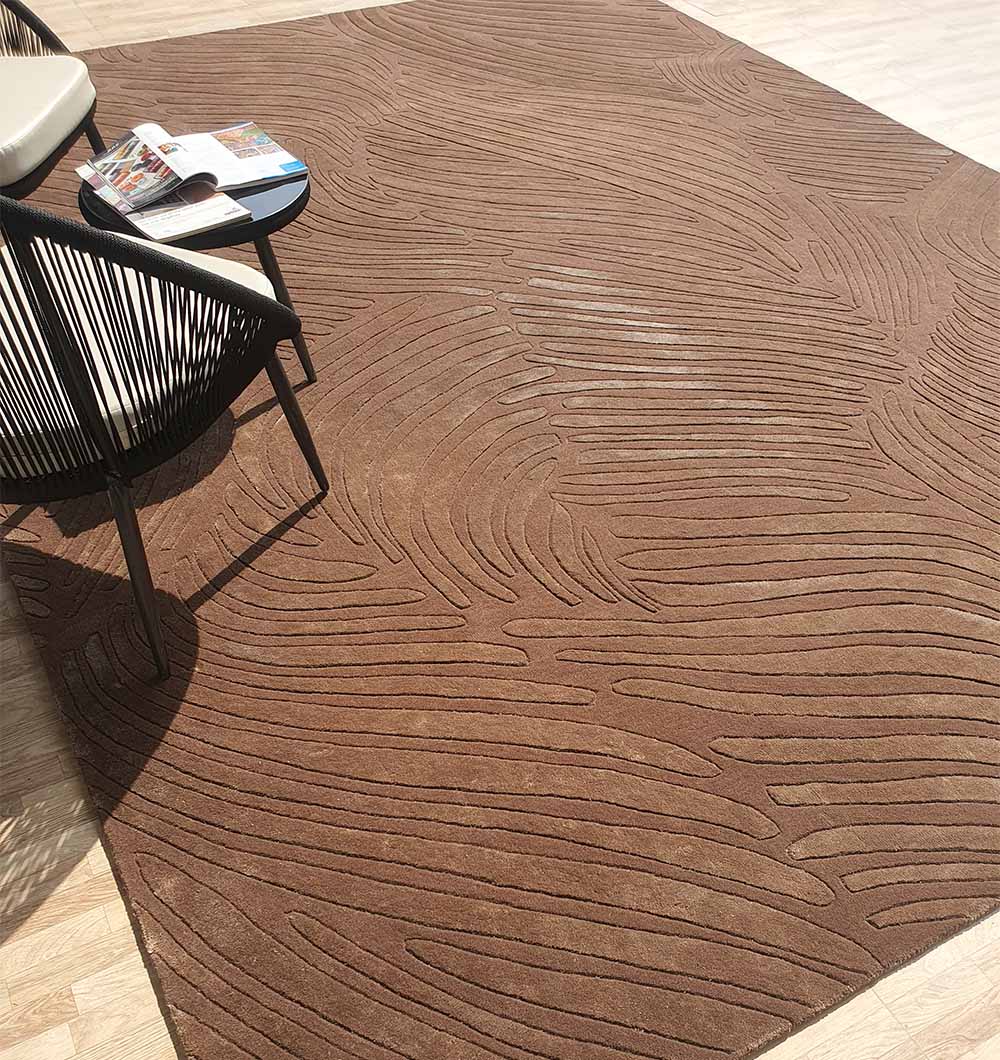 The RAMSHA HOME Premium Quality Handmade Carpet HTWV-79, in chocolate brown with a textured wavy pattern, sits on a light wood floor near a small round black table holding an open magazine and book, beside a modern black woven-back chair.