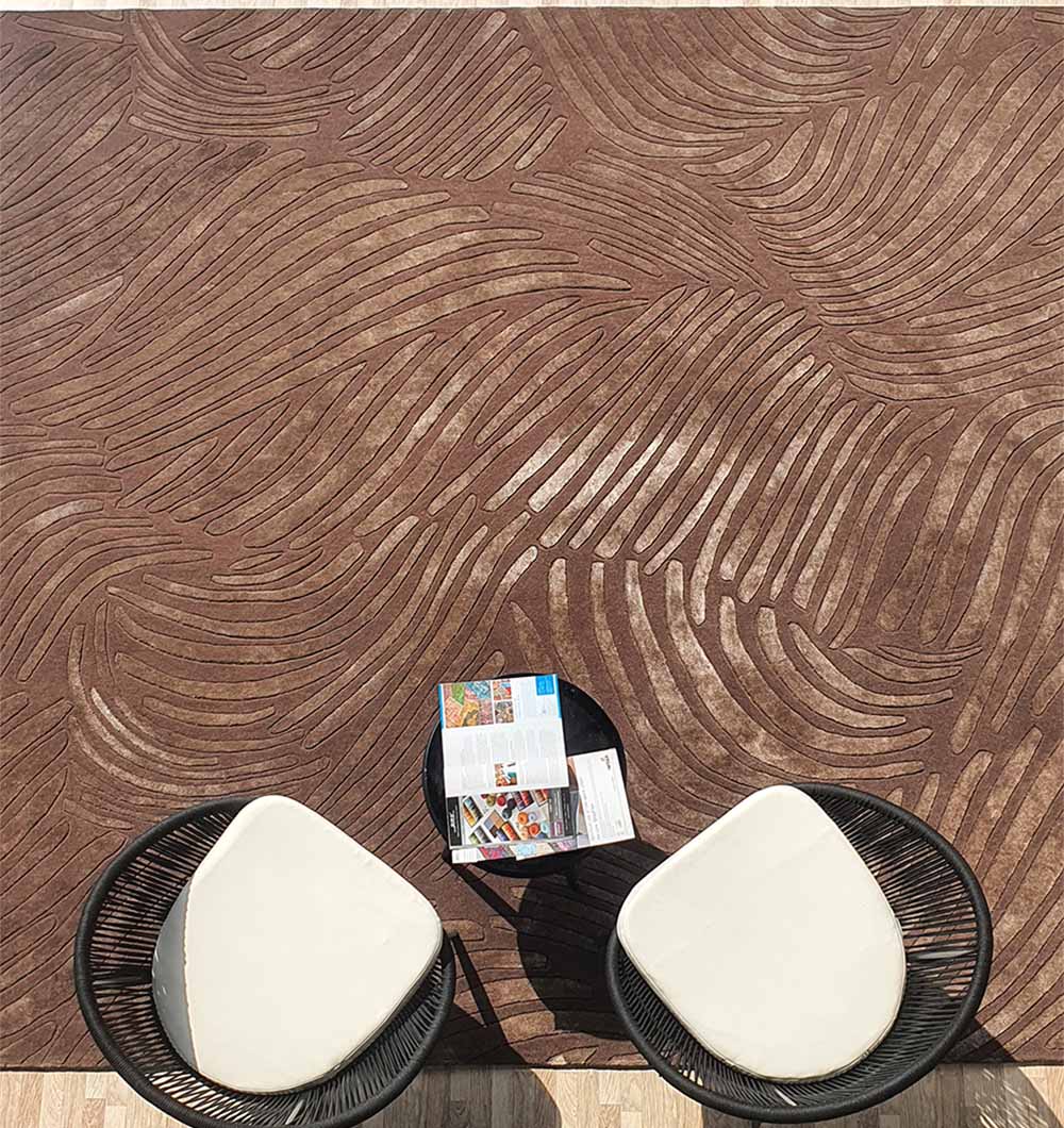 Two white-cushioned black chairs sit by a small table with magazines, all placed on the RAMSHA HOME Premium Quality Handmade Carpet HTWV-79—a chocolate brown, hand-tufted wool rug with elegant wavy textures, seen from above.