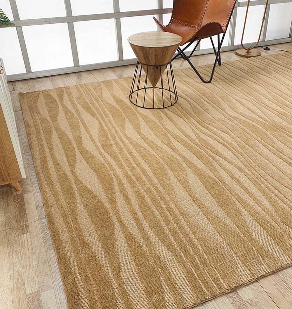 A room with a RAMSHA HOME Rectangle Beige Color Carpet MNR-03, abstract patterns, a wooden tripod side table, a brown leather accent chair, and light wood flooring near large windows.