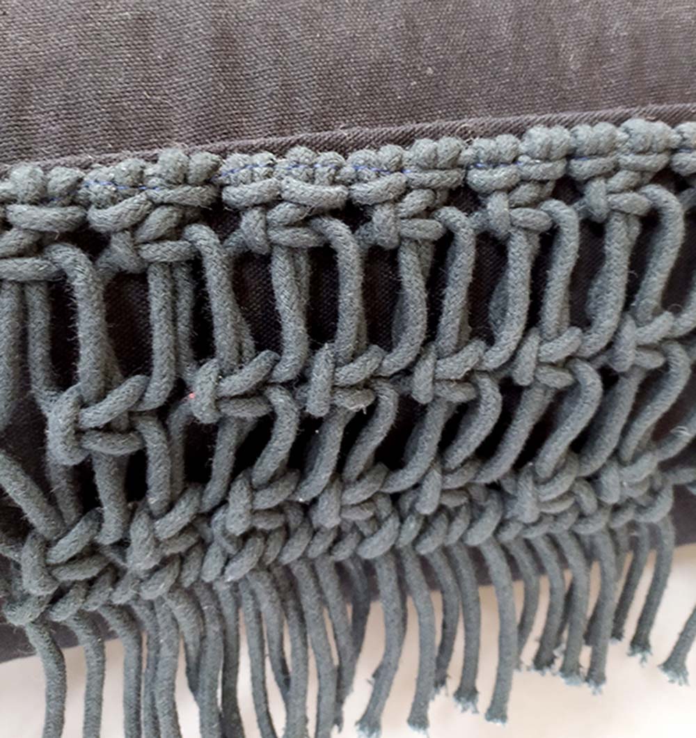 Close-up of dark gray macramé with thick knots and long fringes, set against a plain dark background—pairs perfectly with the RAMSHA HOME Black Cotton Pouf With Fringes PF-044 for comfy seating and added texture.