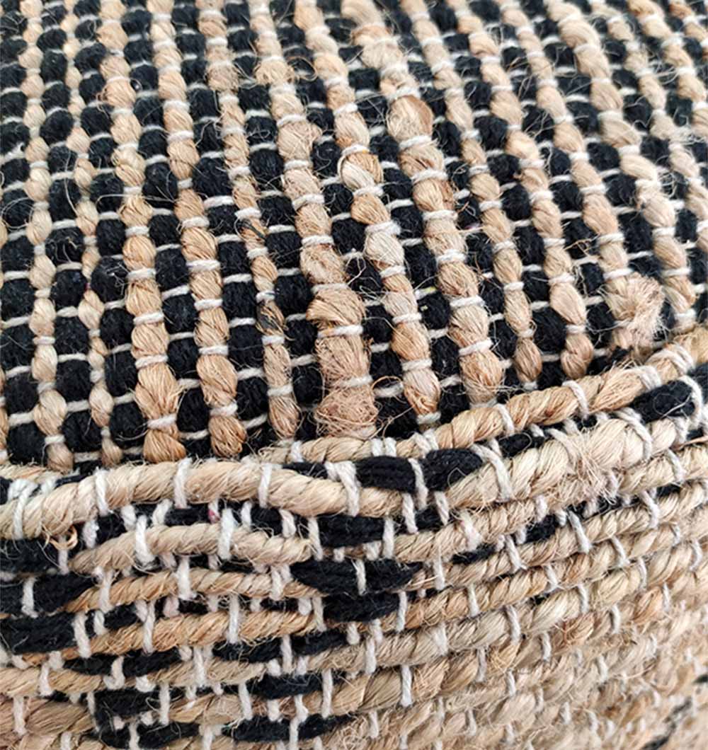Close-up of the RAMSHA HOME Natural Jute Pouf With Leather Handle, showing a pattern of tightly interlaced black and natural jute fibers with a visible horizontal seam.
