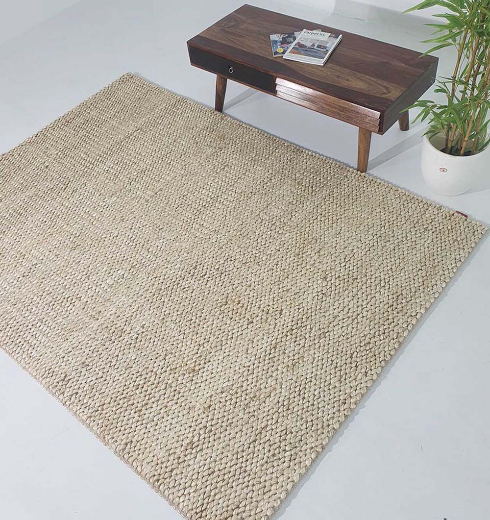 The RAMSHA HOME Bleach Color Woven Floor Rug For Home Decor SR-037 is placed on a white floor next to a wooden coffee table with books and a potted green plant nearby, adding style to your living space.