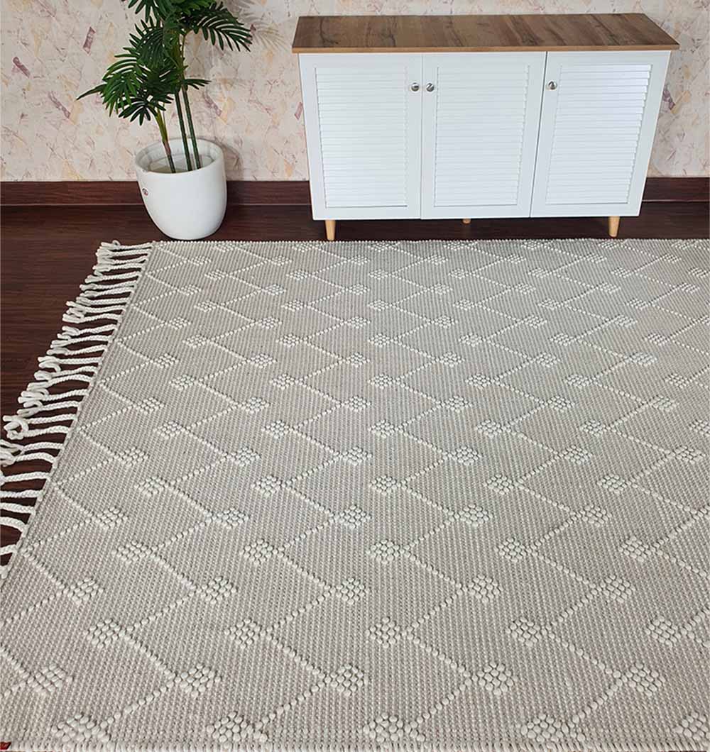 The RAMSHA HOME Designer Room Woven Rug Wool Natural Color SRN-005, featuring a light beige geometric diamond and floral pattern, is placed on a dark wood floor beside a white cabinet and a potted plant.