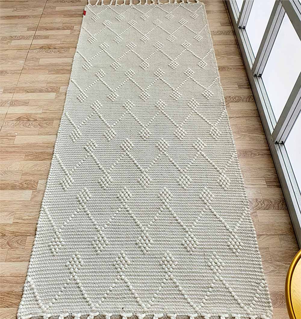 The RAMSHA HOME Designer Room Woven Rug Wool Natural Color SRN-005 features a textured geometric diamond pattern and fringed edges, shown on a light wood floor near large glass windows.