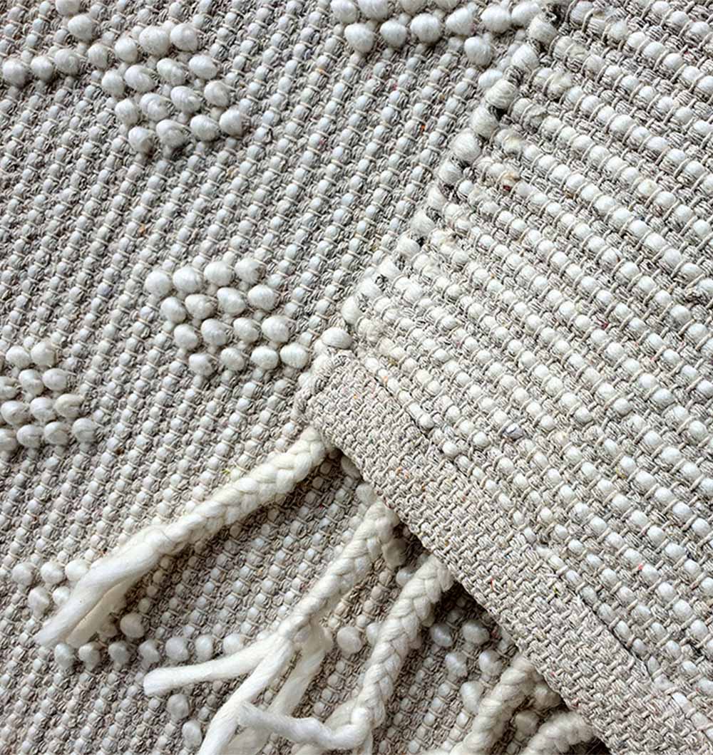 Close-up of RAMSHA HOME’s Designer Room Woven Rug Wool Natural Color SRN-005, highlighting its neutral tones, raised dot pattern, and braided fringe. The grey and ivory design is layered to reveal both the textured surface and fringed edge.