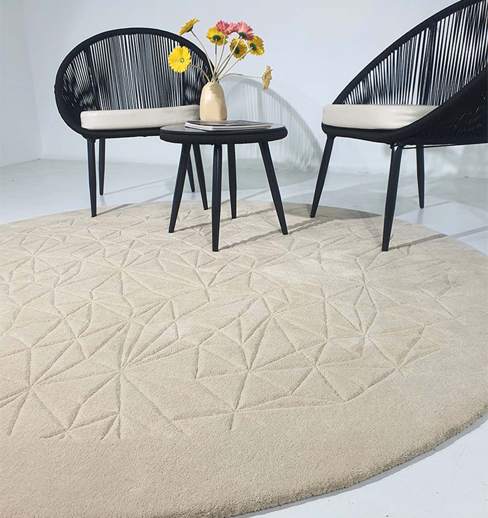 Two black modern chairs and a small round table with a beige vase of flowers sit on the Luxury Home Decor Handmade Carpet – HTW-65 by RAMSHA HOME, showcasing its elegant geometric pattern in a minimalist white room.