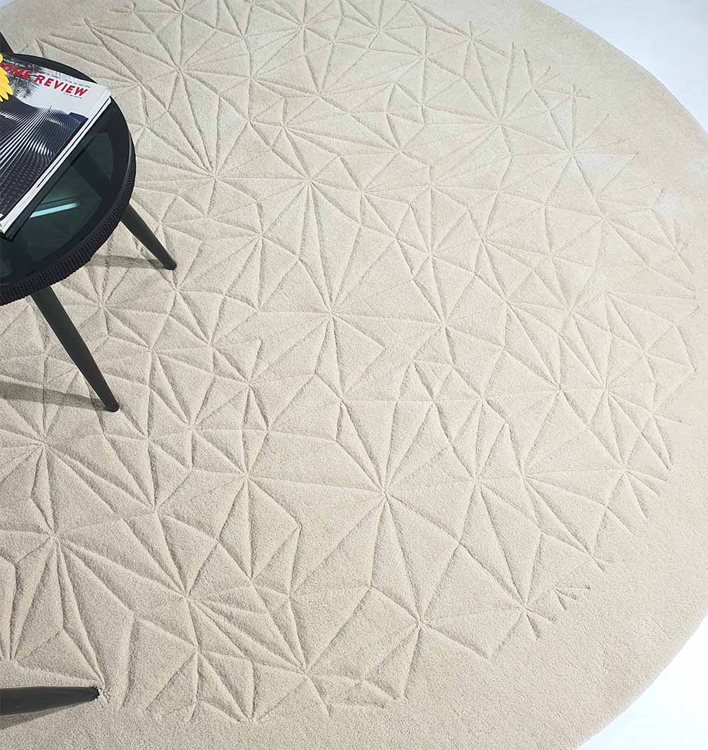 The RAMSHA HOME Luxury Home Decor Handmade Carpet – HTW-65, a round light beige rug with an embossed geometric pattern, is partly visible beneath a black table with magazines.