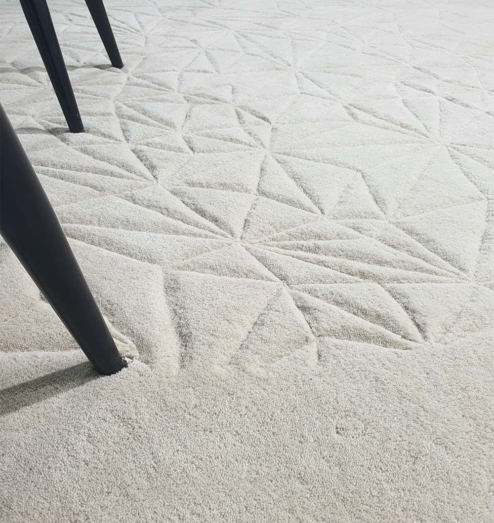 Close-up of the RAMSHA HOME Luxury Home Decor Handmade Carpet – HTW-65, a light beige wool blend rug with a raised geometric pattern; black furniture legs appear on the left side.