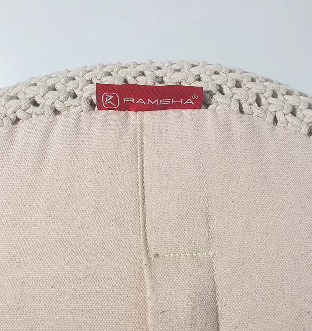 Close-up of the RAMSHA HOME Round Cotton Pouf PF-072 in beige with a textured fabric, woven top edge, and attached red RAMSHA label. Ideal for cozy seating or home décor, shown against a plain light background.