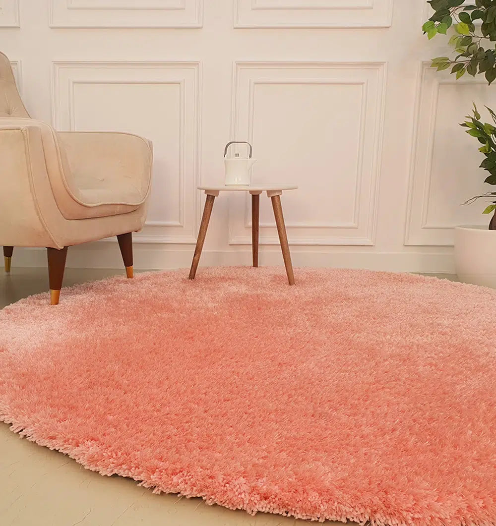The RAMSHA HOME Round Shaped Pink Shaggy Rug - SG 01 brings coziness to the light room, complementing a beige armchair, white side table, and green potted plants by the paneled white wall.
