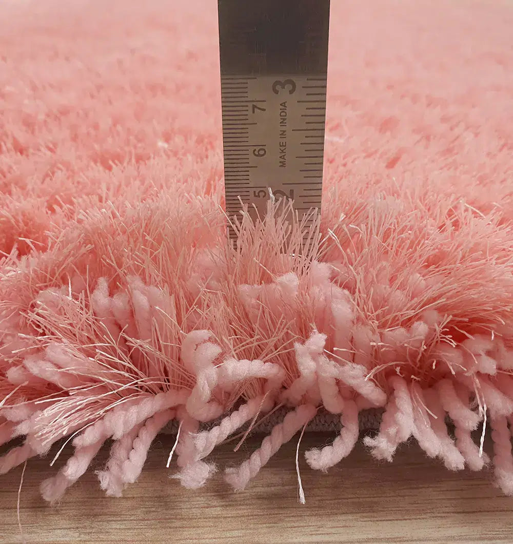 A ruler stands upright on a wooden floor, showing the RAMSHA HOME Round Shaped Pink Shaggy Rug - SG 01 has a plush coral pink pile about 6 centimeters thick.