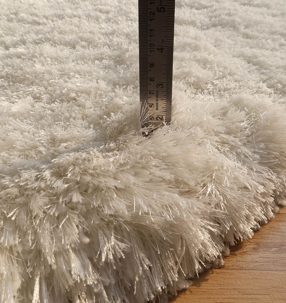 A close-up of the RAMSHA HOME White Color Shape Shaggy Rug - SG 010 (200x300cm) on a wooden floor with a ruler standing upright, showing the plush pile is about 2 inches thick.