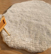 The RAMSHA HOME White Color Shape Shaggy Rug - SG 010 (200x300cm), with its plush pile and irregular shape, is placed on a wooden floor beside the corner of a light wood table.