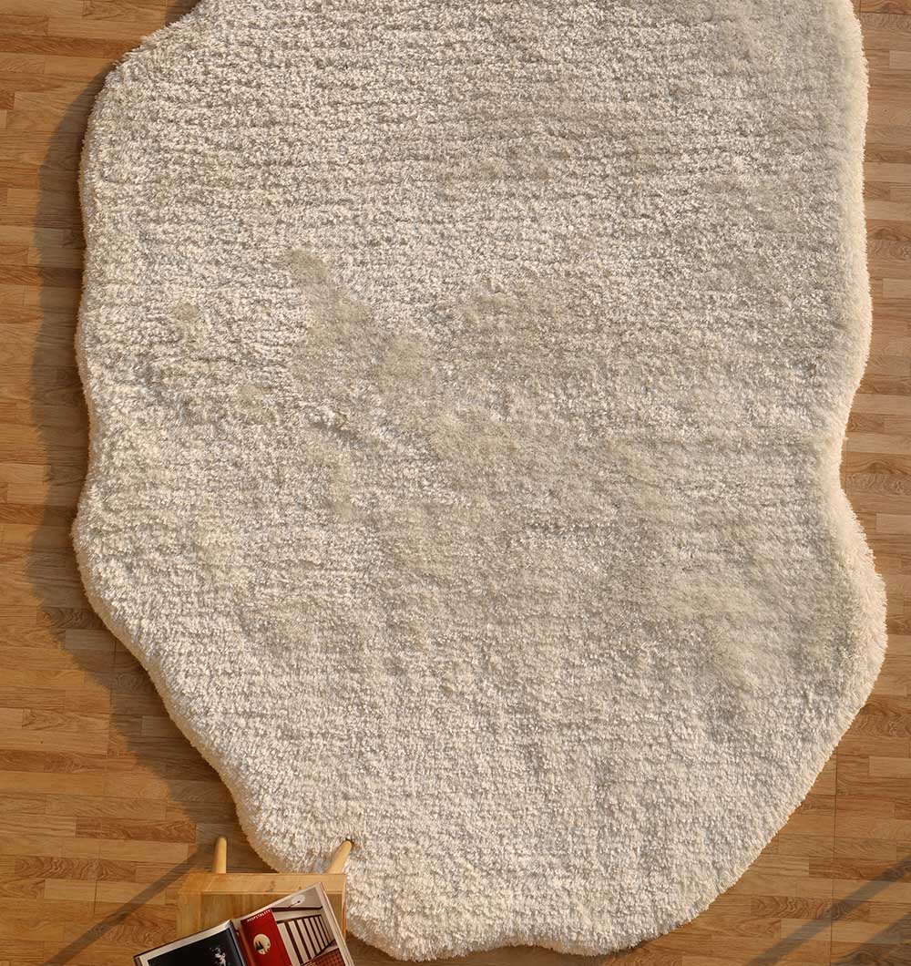 The RAMSHA HOME White Color Shape Shaggy Rug - SG 010 (200x300cm) adds comfort to a wooden floor, with a wooden tray holding magazines and a red cup set on one corner of the fluffy off-white rug.