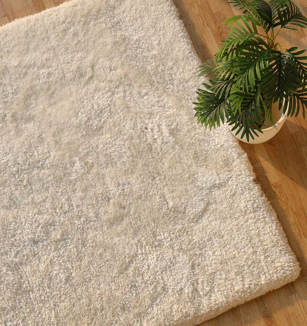 The RAMSHA HOME Plush White Shaggy Rug (SG-011) lies on a wooden floor, its soft modern texture enhanced by the presence of a green potted plant in the top right corner.
