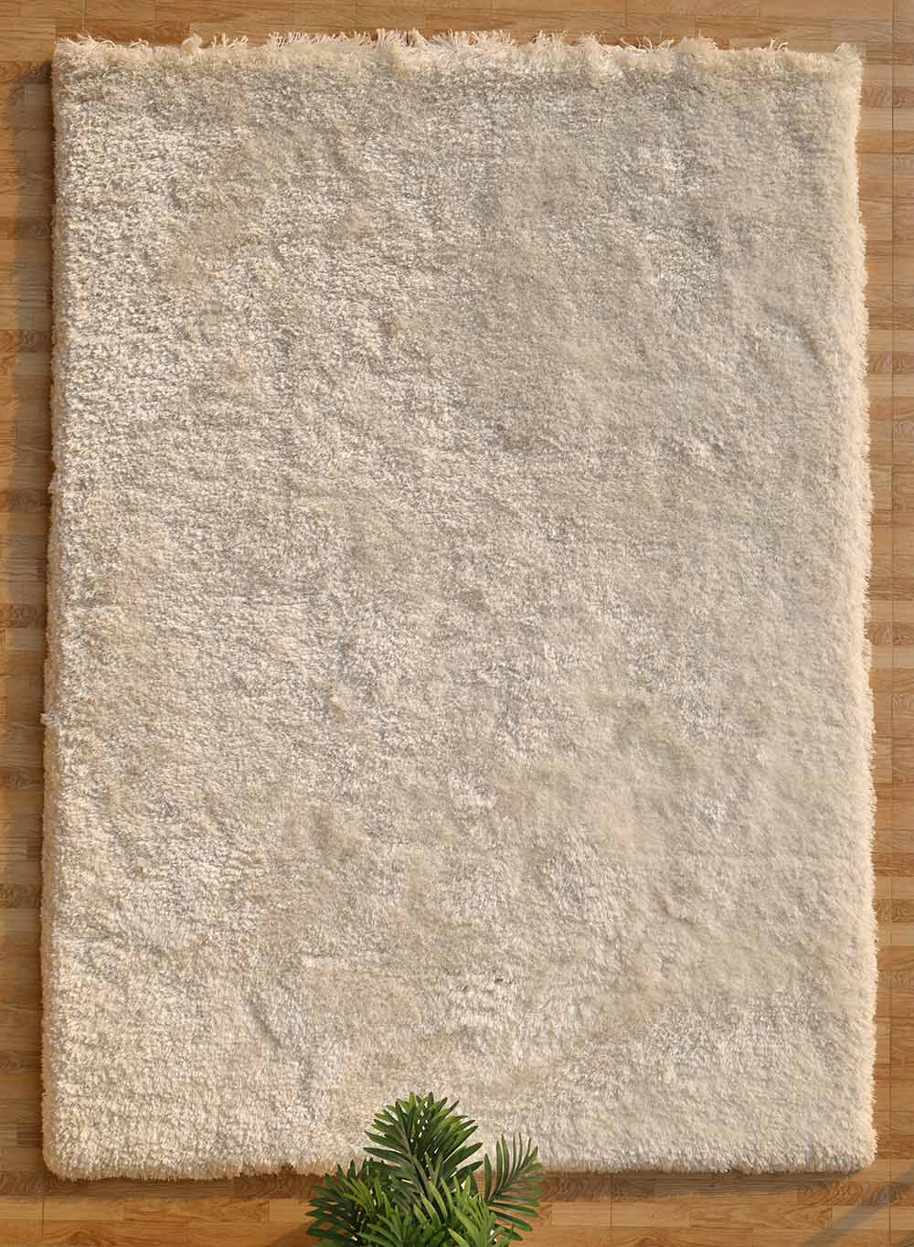 The RAMSHA HOME Plush White Shaggy Rug for Modern Living Room Decor (SG-011) lies on a wooden floor, its soft texture adding warmth, while a green plant appears at the bottom edge of the image.