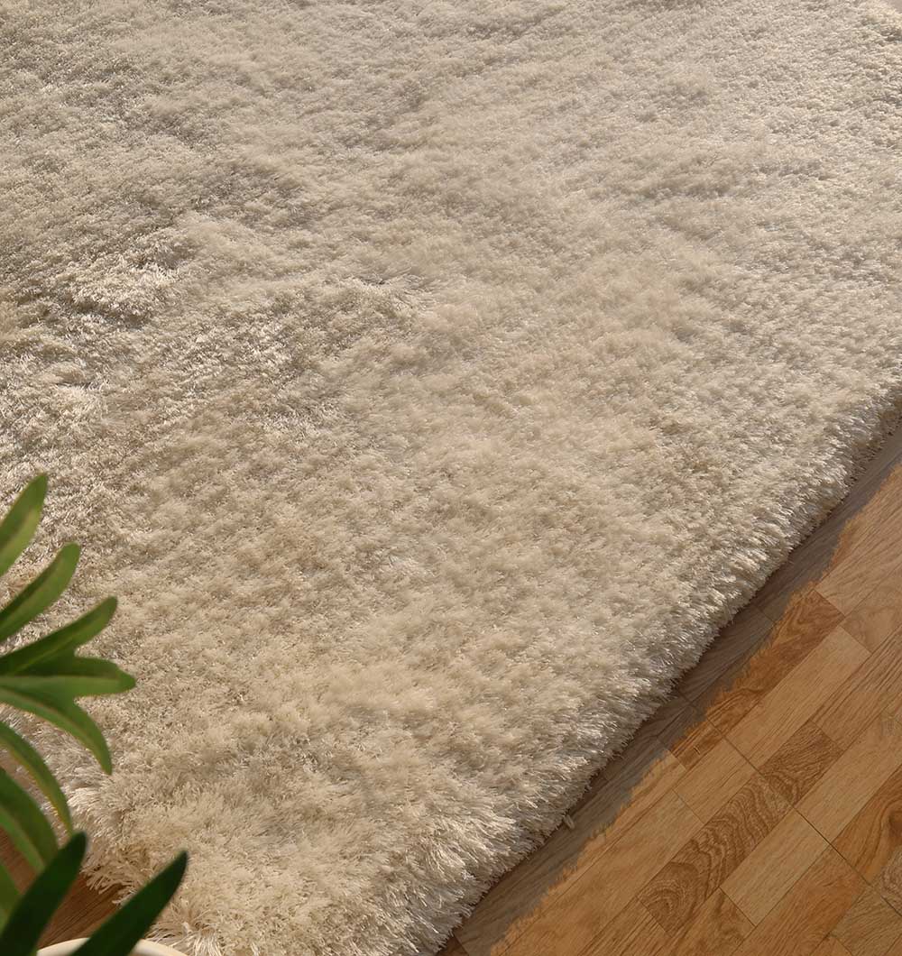 A close-up of the RAMSHA HOME Plush White Shaggy Rug (SG-011) on a wooden floor, featuring soft cream hues with a green plant in the corner—perfect for modern living room decor.