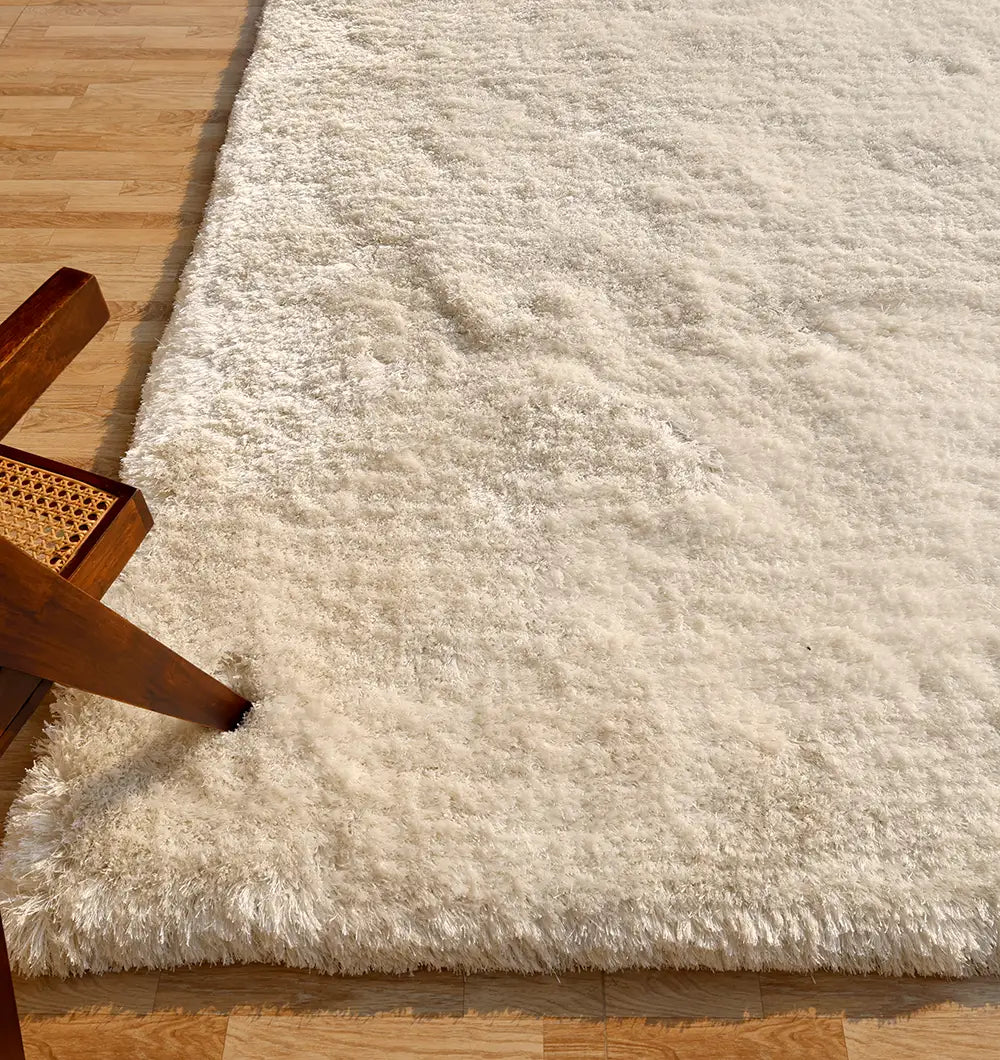 The RAMSHA HOME Plush White Shaggy Rug for Modern Living Room Decor (SG-011) rests on a light wood floor, with a wooden chair featuring a woven cane seat visible at the left edge of the image.