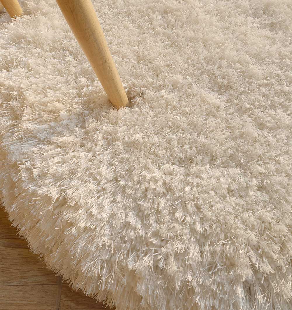 Close-up of the RAMSHA HOME Decorative Shaggy Rug White Color - SG-012, featuring a thick pile and shag finish, with two light wooden furniture legs on it and part of a light wooden floor in the corner.
