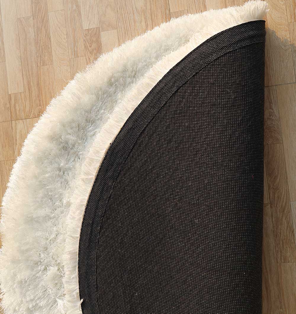 The Decorative Shaggy Rug White Color - SG-012 by RAMSHA HOME is partially folded on a light wood floor, showing its textured black underside.