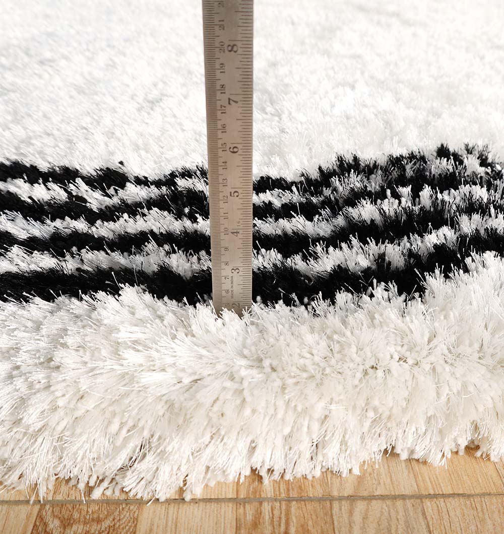 A metal ruler measures the pile of the RAMSHA HOME White & Black Shaggy Rug for Modern Living Room Decor (model SG-013), highlighting its plush thickness on a wooden floor.