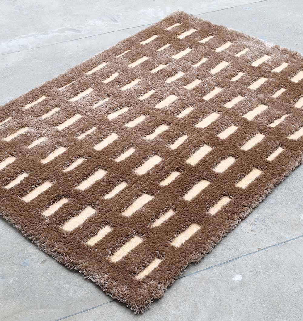The RAMSHA HOME Modern Shaggy Rug For Living Room SG 015 (170x240 CM) is a rectangular brown and beige geometric rug with vertical beige rectangles on a brown background, displayed on a light gray concrete floor.