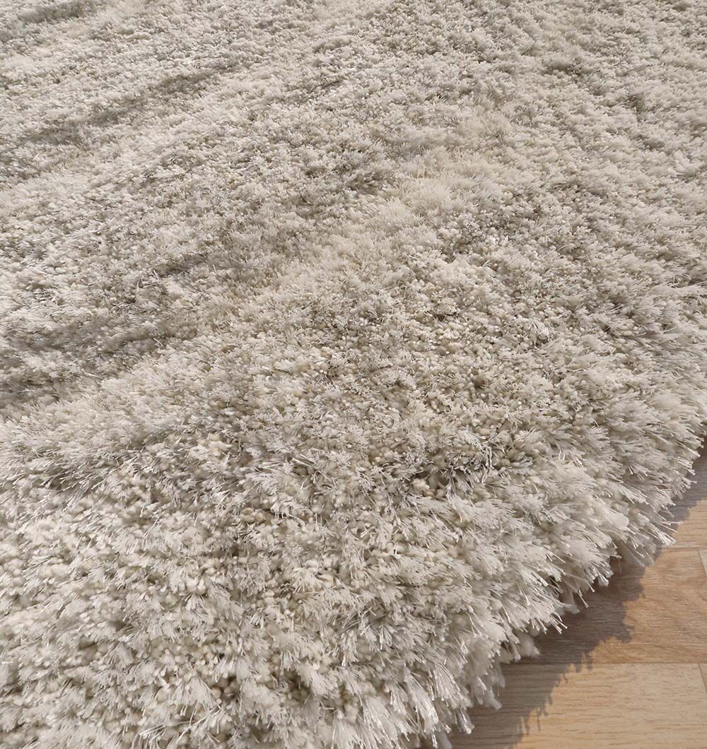 A close-up of the RAMSHA HOME Wavy Texture Shape Rug for Living Room - SG 016 (200 x 300 cm), featuring plush light beige shaggy fibers in an irregular shape, placed on a light wooden floor.