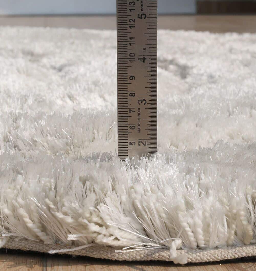 A metal ruler measures the thickness of the RAMSHA HOME Wavy Texture Shape Rug for Living Room - SG 016 (200 x 300 cm), showing the plush beige rug is just under 2 inches thick on a wooden floor.