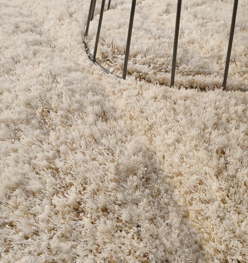 Close-up of the RAMSHA HOME Shaggy Shape Rug for Living Room - SG 017 (200x300 cm), featuring dense, cream-colored, plush fibers and thin metal rods curving along the upper edge.