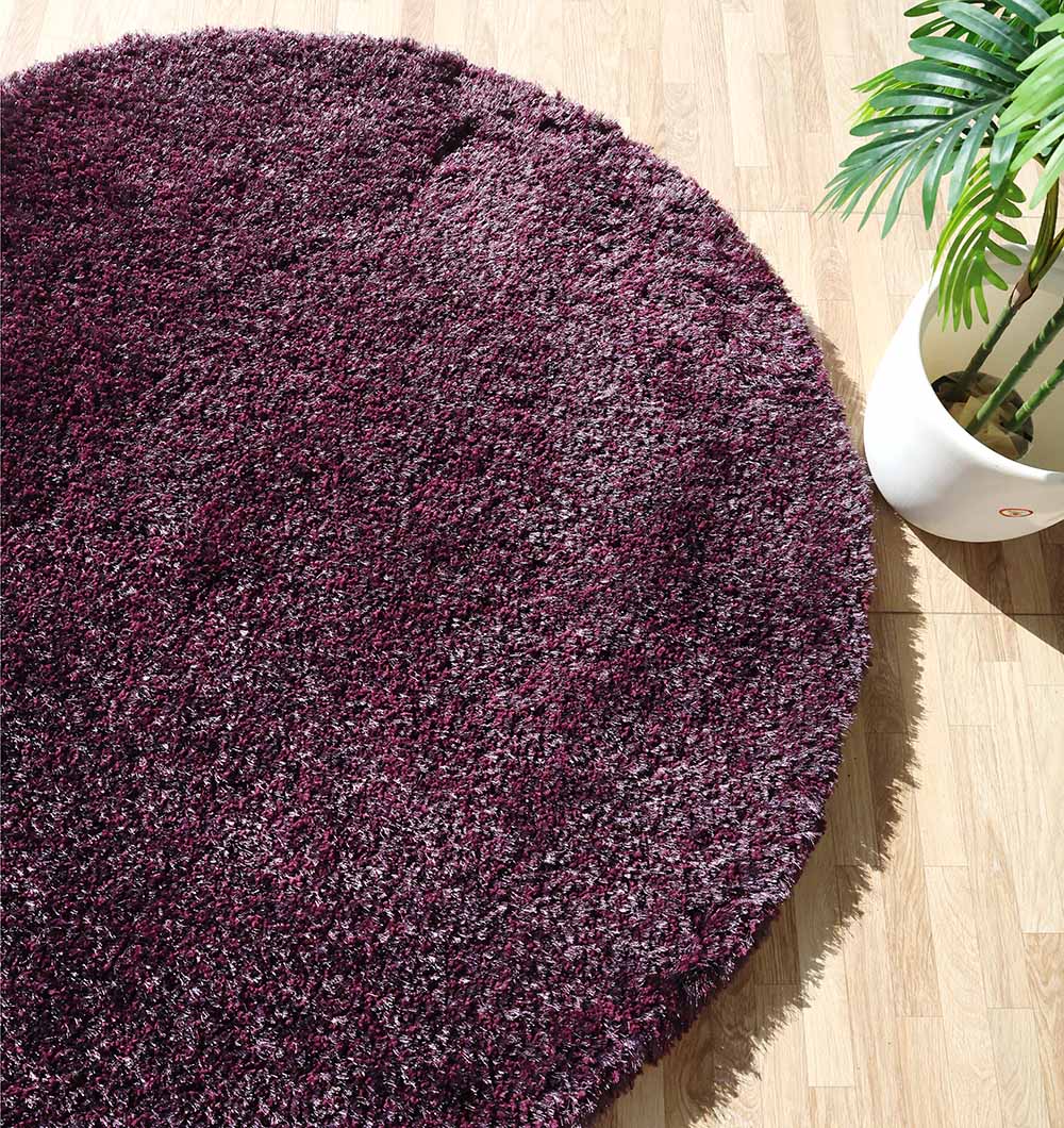 The RAMSHA HOME Shaggy Rug for Living Room - SG 019, a round purple accent rug, is displayed on a light wood floor beside a potted green plant.