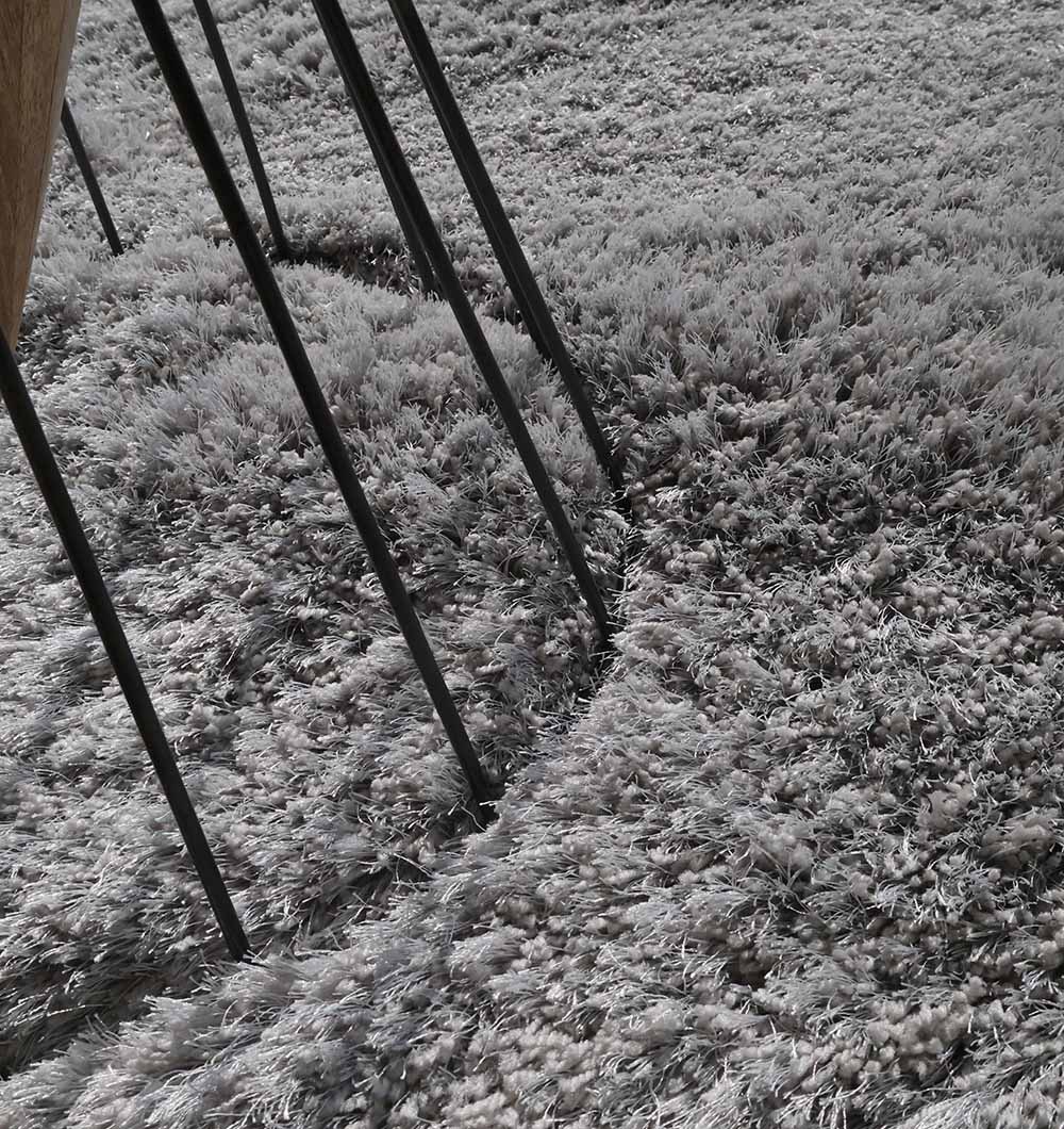 The thin black metal legs of a furniture piece rest on the RAMSHA HOME Shaggy Shape Rug for Living Room - SG 020 (175x300 cm), leaving visible indentations in its soft, plush surface.