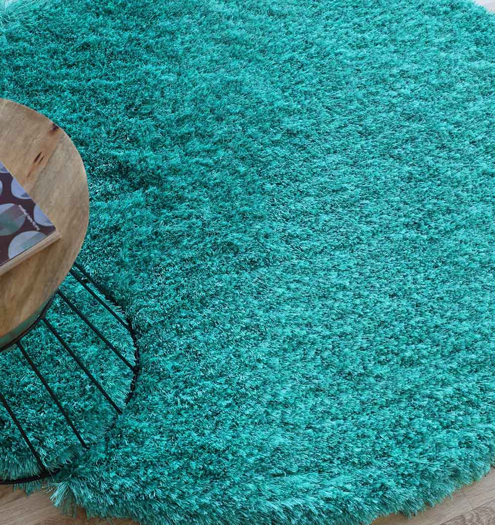 A close-up of the RAMSHA HOME Turquoise Fluffy Shaggy Round Shape Area Rug SG 021 on a wooden floor, with part of a round wooden table—showcasing the rug’s invitingly soft texture.