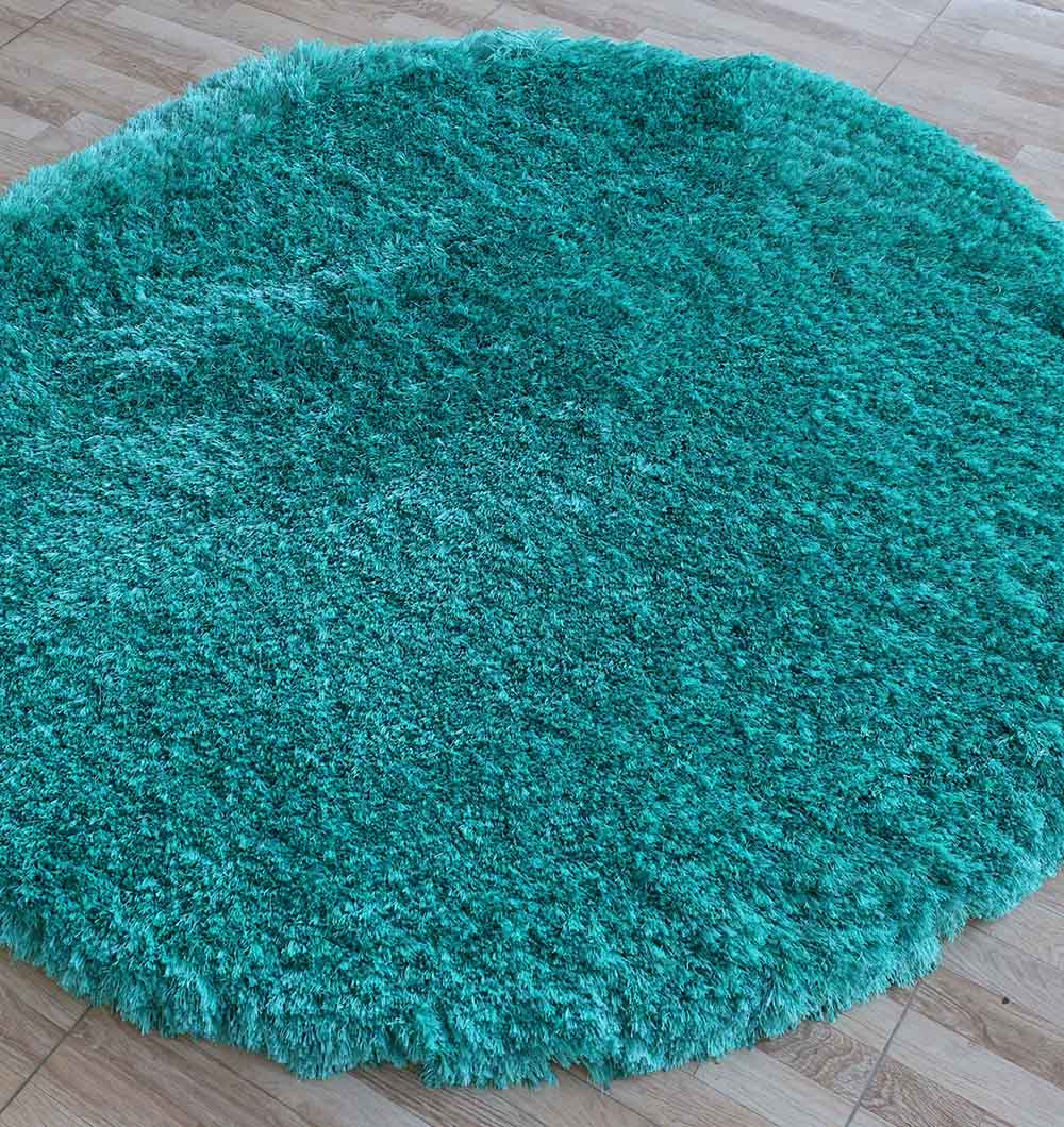 The RAMSHA HOME Turquoise Fluffy Shaggy Round Shape Area Rug SG 021, with its plush texture, adds a vibrant pop of color and softness to the light wood floor, creating a striking contrast against the smooth brownish surface.