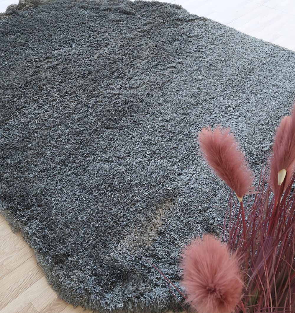 The RAMSHA HOME Shaggy Shape Rug for Living Room - SG 022 (200x300 cm) in plush gray rests on a light wooden floor, while pink pampas grass in a vase is partly seen in the bottom right corner.