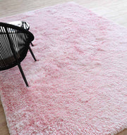 The RAMSHA HOME Light Pink Color Dining Room Shaggy Rug - SG 02 lies on a light wooden floor, with a black chair partially visible at the rug's edge.