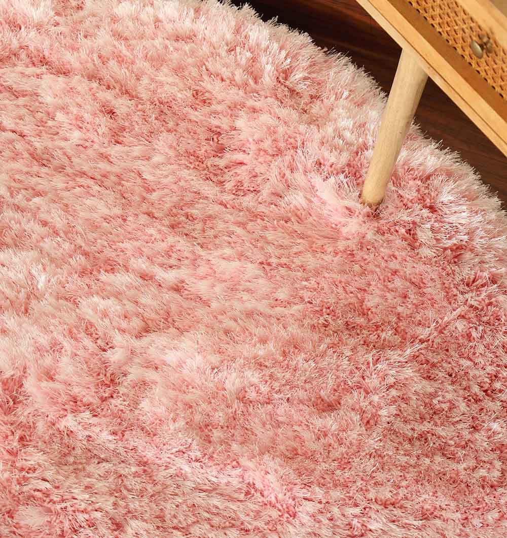 A close-up of the Light Pink Color Home Decor Round Shaggy Rug - SG 02, showcasing its fluffy texture with a hint of a wooden furniture leg visible in the corner.