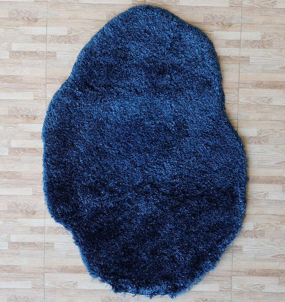 The RAMSHA HOME Blue Color Home Decor Shaggy Rug - SG 024, with its soft shaggy texture and irregular round shape, is placed on a light-colored, wood-patterned floor.