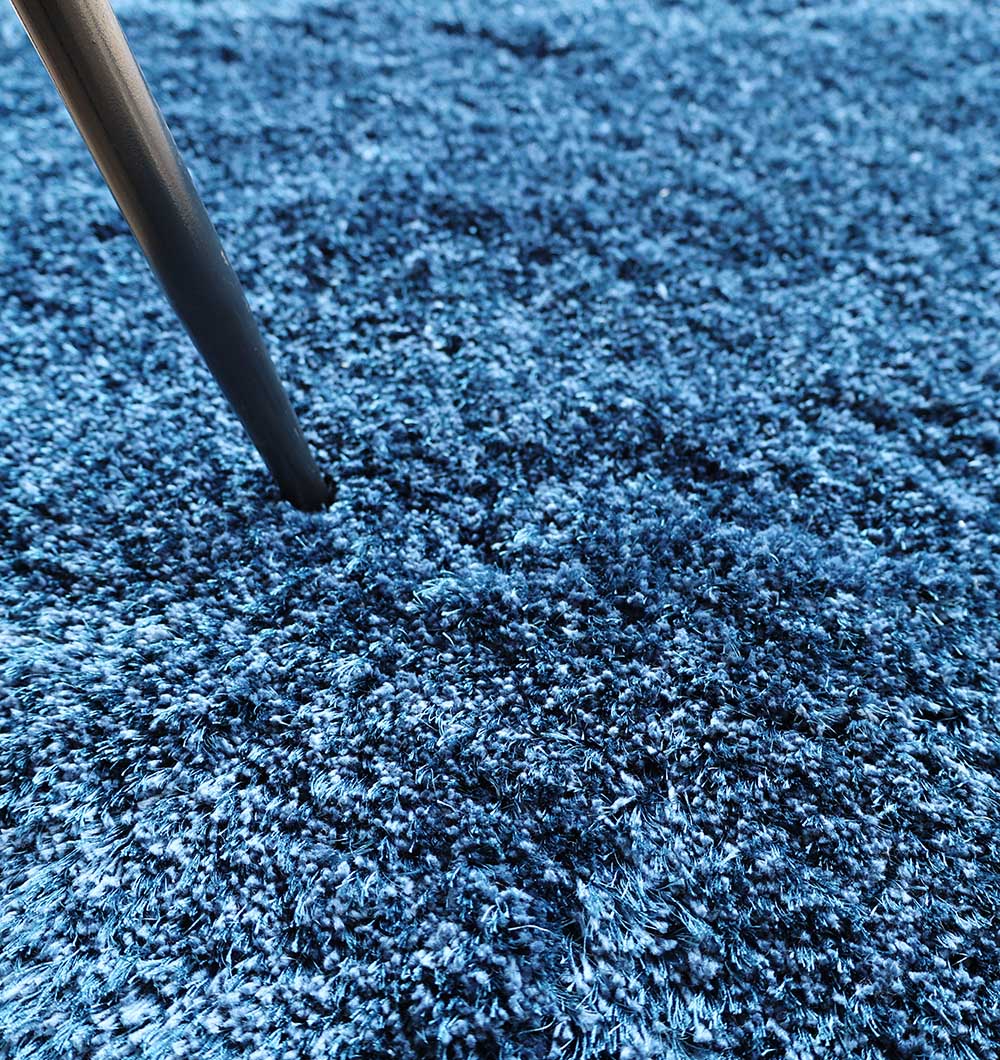 A close-up of a metal furniture leg pressing into the thick, textured surface of the Blue Color Home Decor Shaggy Rug - SG 024 by RAMSHA HOME.