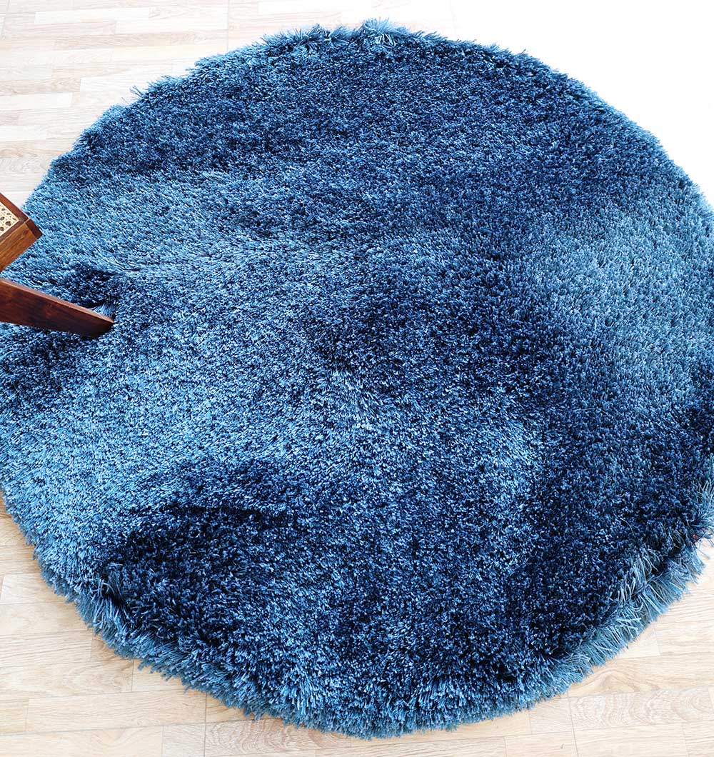 The RAMSHA HOME Blue Color Home Decor Shaggy Rug - SG 024, featuring varied blue shades, adds soft texture to a light wooden floor; a wooden chair appears in the upper left corner.