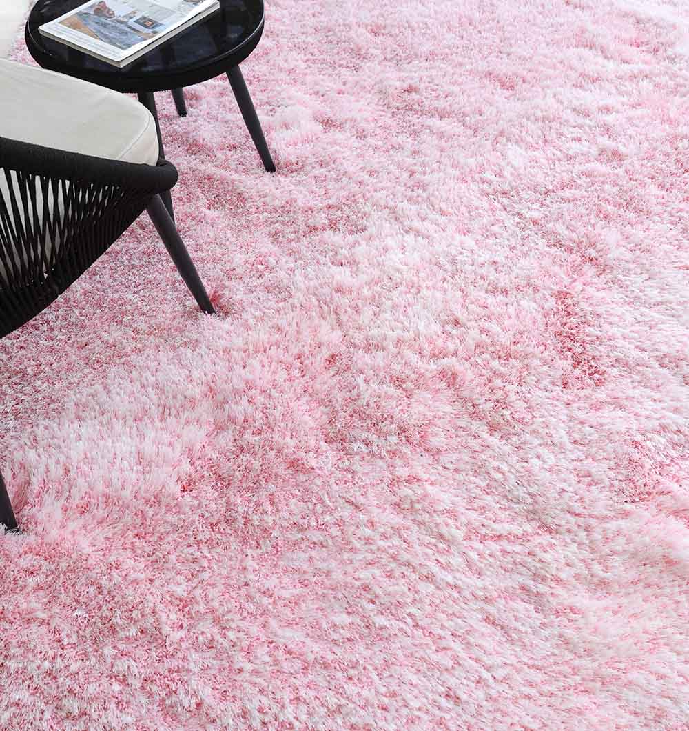 A close-up of the RAMSHA HOME Light Pink Color Dining Room Shaggy Rug - SG 02, featuring white accents, with a black round side table and part of a chair visible in the corner.