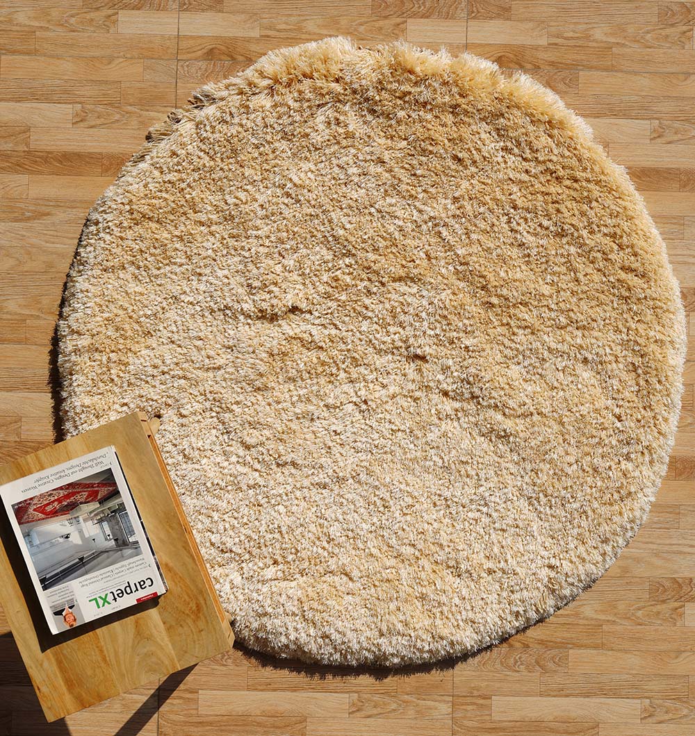 The RAMSHA HOME Shaggy Rug for Living Room - SG 026, a round ivory piece, sits on a light wood floor near a wooden table with an open magazine on top.