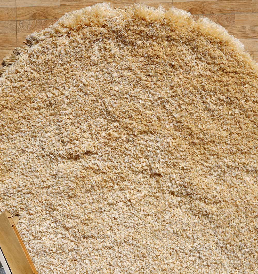 The RAMSHA HOME Shaggy Rug for Living Room - SG 026 in beige, featuring a plush shaggy texture, covers most of a wooden floor. The rounded edge is prominent, with a glimpse of the floor and an object’s corner visible at the bottom left.